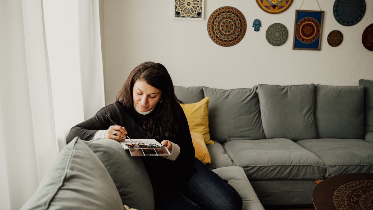 Woman drawing in a cozy living room with artistic wall decor and soft lighting.